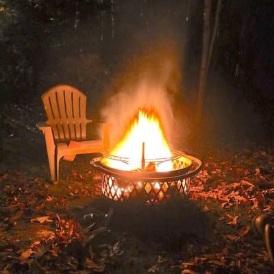 A fire burning in the fire pit beside an Adirondack chair at Oliver's Outlook, at night